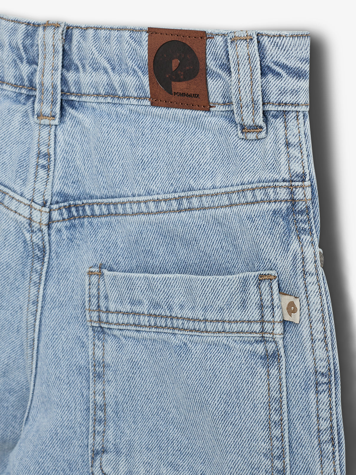 Light blue denim shorts feature a leather patch with a "P" logo and "POMPdeLUX" text above the back pocket, set on a white background.