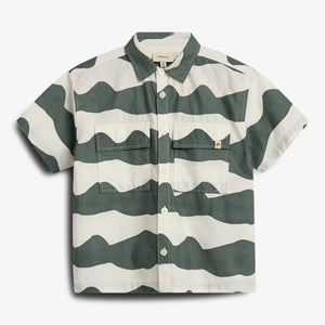 A short-sleeved button-up shirt features bold, wavy green and white stripes, with two front pockets. It is displayed against a plain white background.