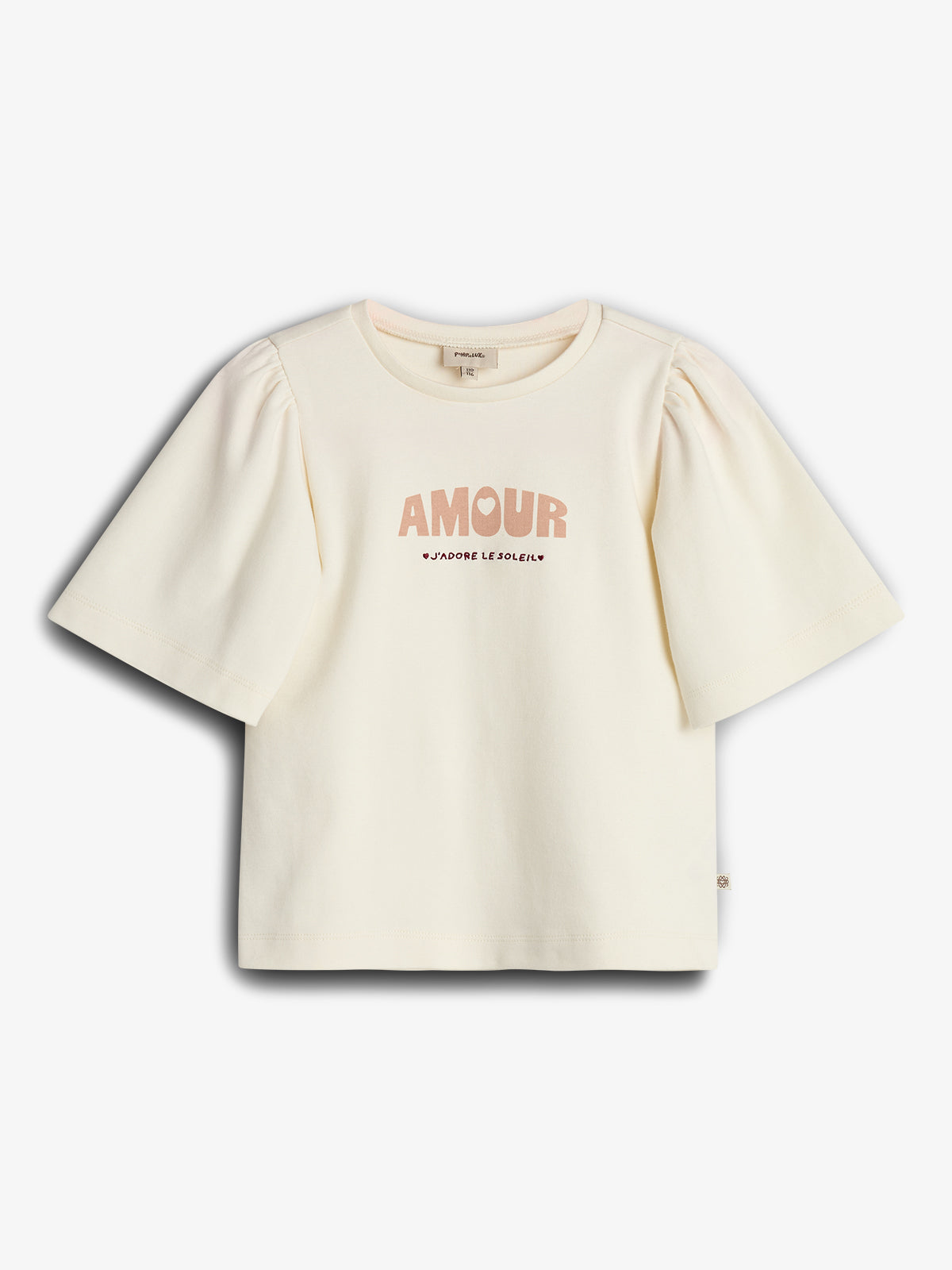 Cream-colored T-shirt featuring puffed sleeves, displays text "AMOUR" and "J’ADORE LE SOLEIL." The shirt is laid flat against a plain white background.