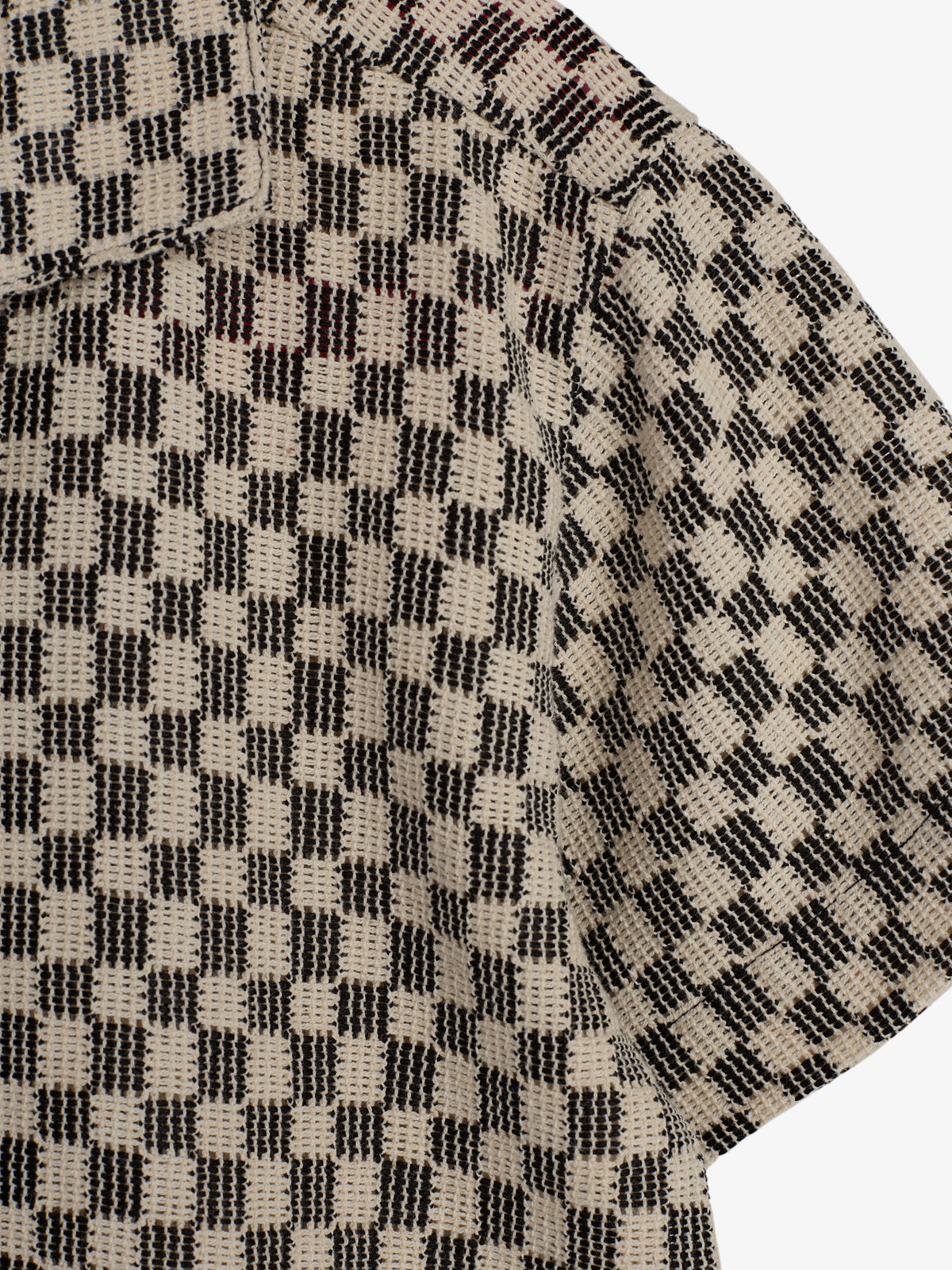 A checkered-patterned fabric with a beige and black woven design, shown in close-up, forming part of a garment with a collar. The background is plain white.
