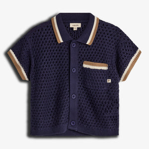 A navy blue, short-sleeved, knitted cardigan with button closure and striped collar and sleeves, features a pocket with beige and white accents. Label reads "pimaluLino." Background is plain white.