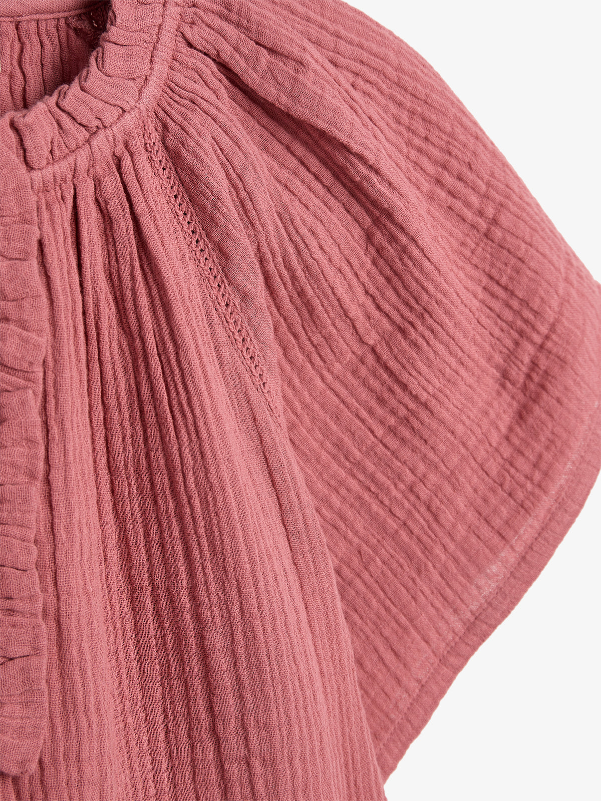 A textured pink fabric features pleats and gathers, creating a detailed, flowing design. The fabric, possibly part of a garment, is captured against a plain white background.