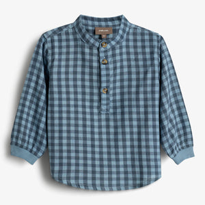 A blue plaid long-sleeved shirt with a mandarin collar and three brown buttons is displayed against a plain white background. Label text reads: "POMP de LUX, 86."