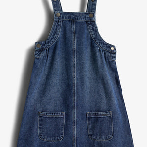A blue denim pinafore dress with two straps and front pockets, laid flat against a white background.