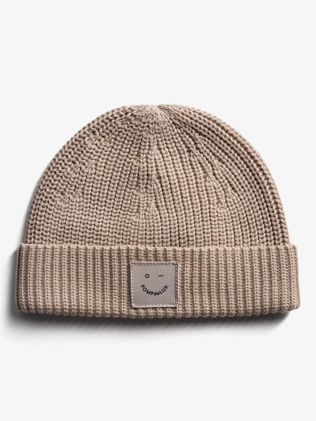 A beige knitted beanie displaying a simple, embroidered smiley face patch with text "POMPdeLUX" on its fold-up edge, against a plain white background.