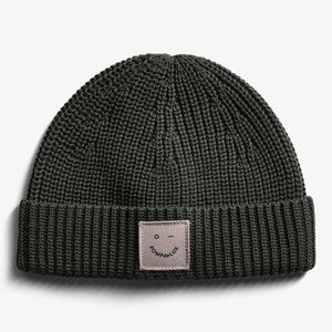 A knitted dark green beanie, featuring a folded brim with a square patch labeled "POMPdeLUX" on a plain white background.