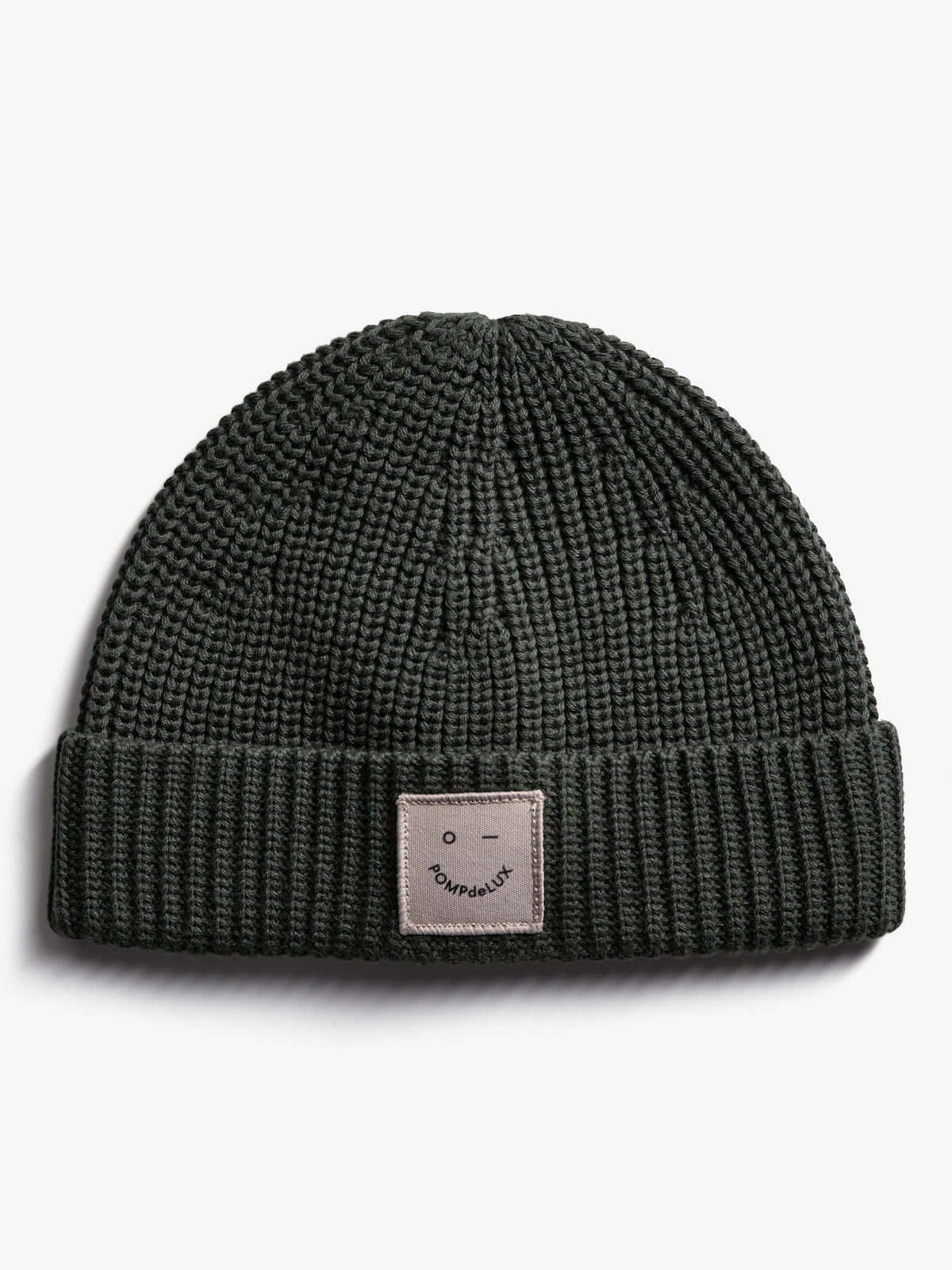 A knitted dark green beanie, featuring a folded brim with a square patch labeled "POMPdeLUX" on a plain white background.