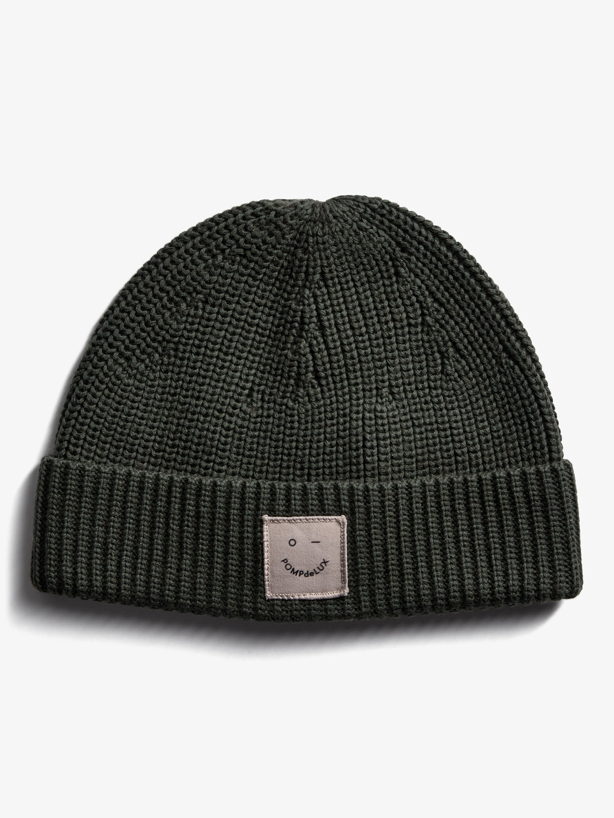A knitted dark green beanie displays a small patch with a smiley face and the text "POMPdeLUX" against a plain white background.