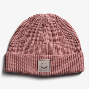 A pink knit beanie with a folded brim, featuring a patch showing a simple face and the text "POMPEDE LUX," set against a plain white background.